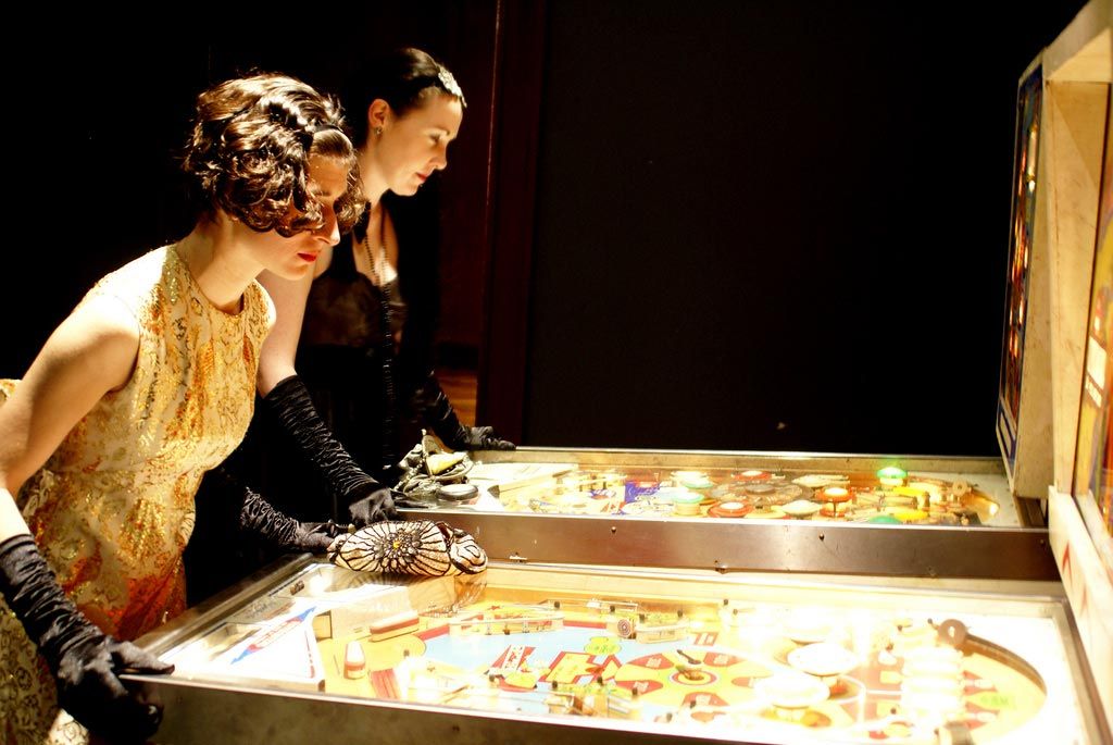 Fancy gals playing vintage pinball machines